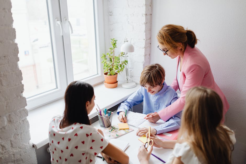 A teacher assists students with schoolwork around a desk in a bright classroom